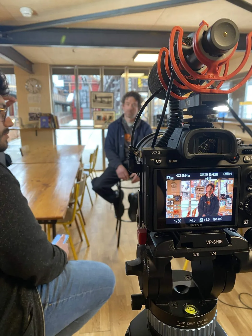 Une caméra filme une personne attablée dans un café-atelier